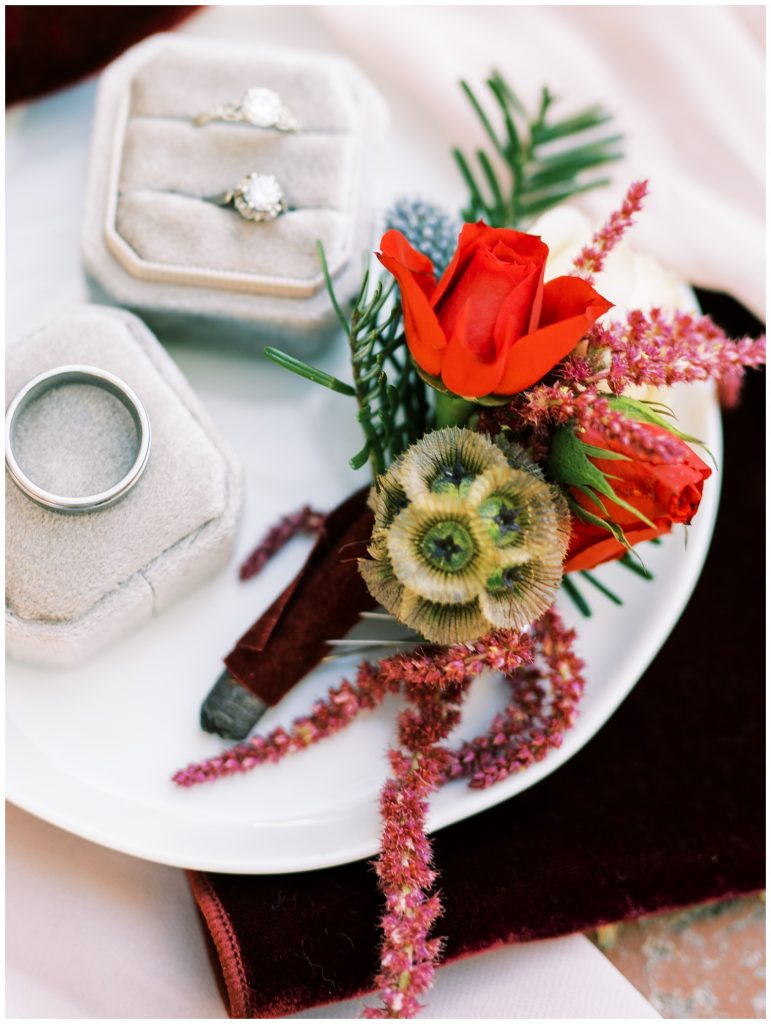 Close-up photo of a groom's boutonnière, with small red rose and pine needles