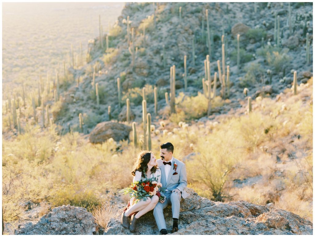 Wedding couple sitting on a rock with Saguaros in the background